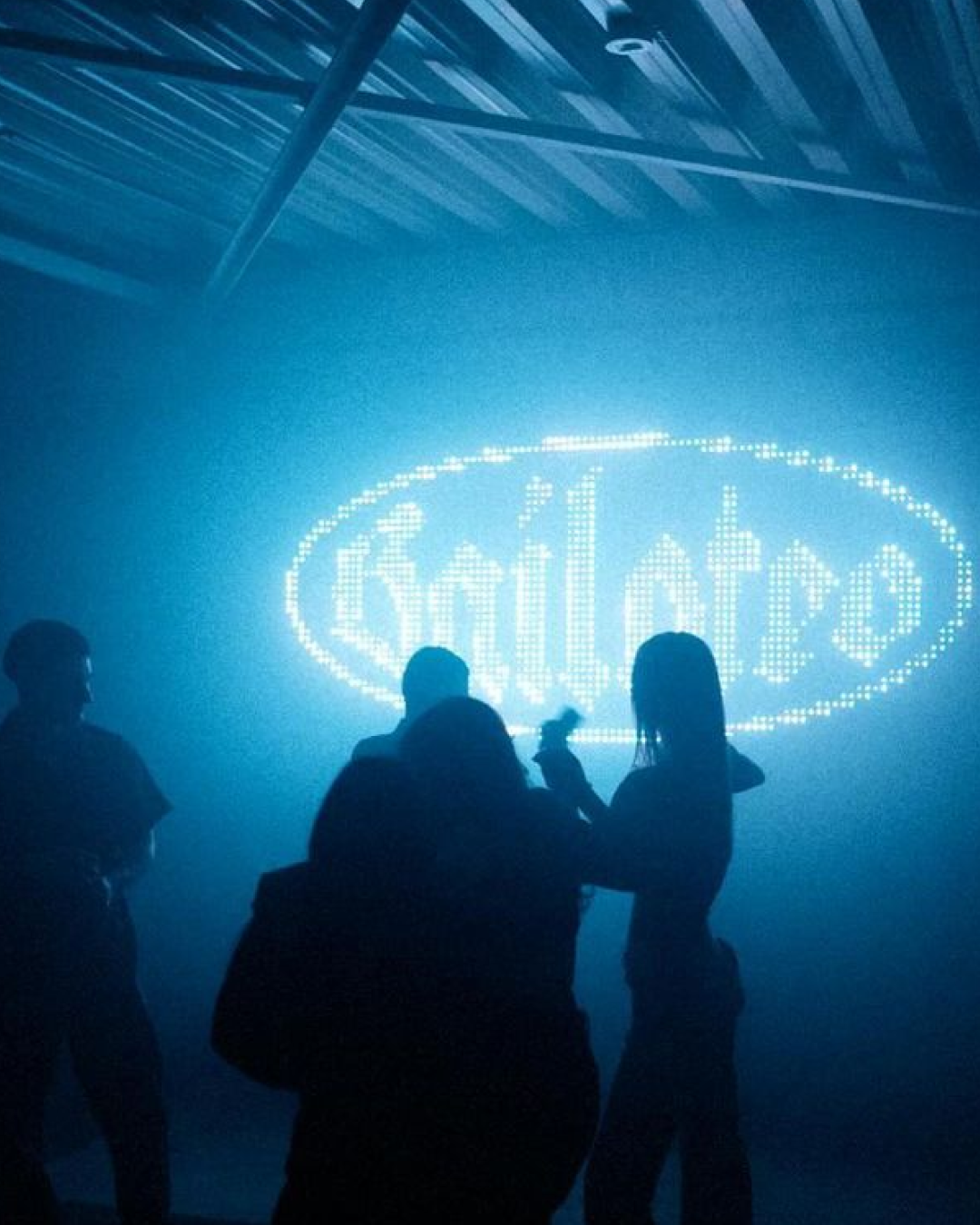 Silhouettes of party guests in fog in front of a LED Bailoteo logo